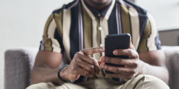 Hombre con camiseta a rayas usando su teléfono móvil mientras sigue contenido digital.